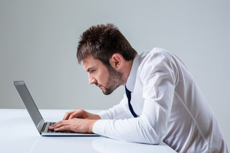 nerd young male typing on laptop. It uses a computer while sitting at a table. Office clothingの写真素材