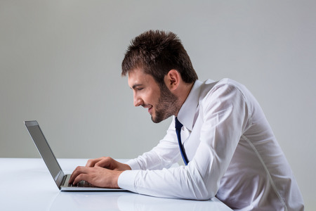 nerd young male smiling and typing on laptop. It uses a computer while sitting at a table. Office clothingの写真素材