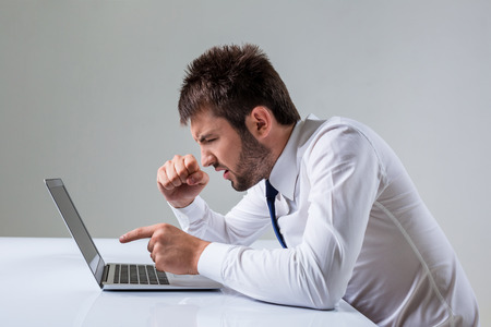 the young man is nervous and poke a finger. It uses a computer while sitting at a table. Office clothingの写真素材