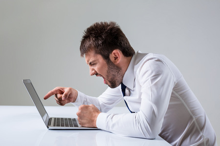 the young man is nervous and poke a finger. It uses a computer while sitting at a table. Office clothingの写真素材