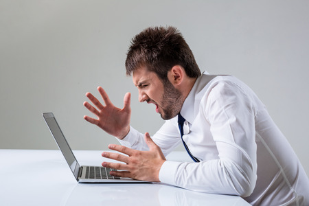 the young man is nervous. It uses a computer while sitting at a table. Office clothingの写真素材