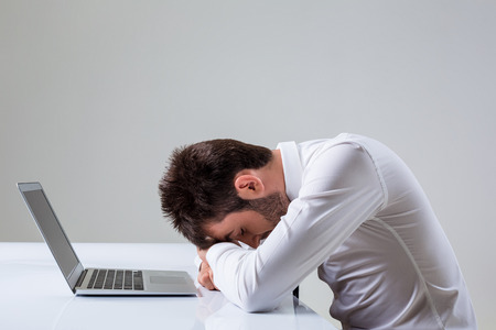 the young man was tired, and laid his head on the keyboard. It uses a laptop computer while sitting at a table. Office clothingの写真素材