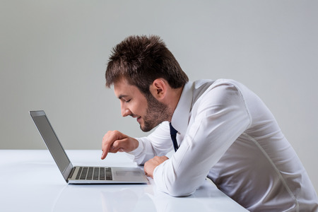 young man presses the keyboard on a laptop bully. It uses a computer while sitting at a table. Office clothingの写真素材