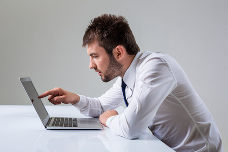 young man presses the laptop. It uses a computer while sitting at a table. Office clothingの写真素材