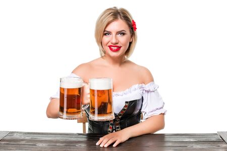 Beautiful young blond girl in dirndl drinks out of oktoberfest beer stein. Isolated on white background. sits by the tableの写真素材
