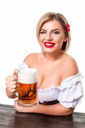 Beautiful young blond girl in dirndl drinks out of oktoberfest beer stein. Isolated on white background. sits by the tableの写真素材