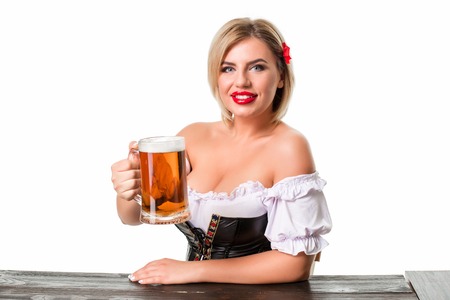 Beautiful young blond girl in dirndl drinks out of oktoberfest beer stein. Isolated on white background. sits by the tableの写真素材