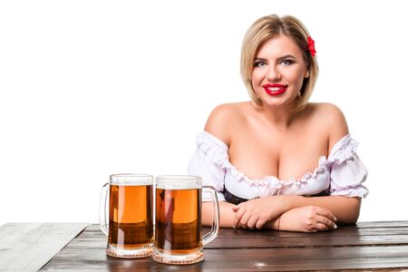 Beautiful young blond girl in dirndl drinks out of oktoberfest beer stein. Isolated on white background. sits by the tableの写真素材