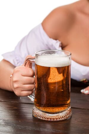 Beautiful young blond girl in dirndl drinks out of oktoberfest beer stein. Isolated on white background. sits by the table. close-up mugの写真素材
