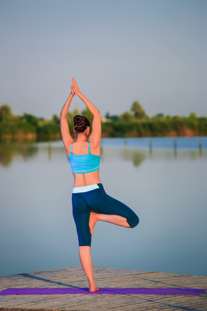 girl doing yoga exercises on the river bank at sunsetの写真素材
