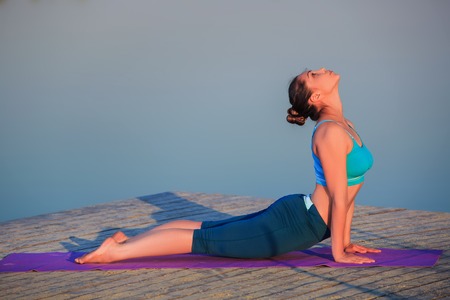 girl doing yoga exercises on the river bank at sunsetの写真素材