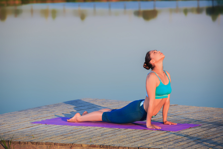 girl doing yoga exercises on the river bank at sunsetの写真素材