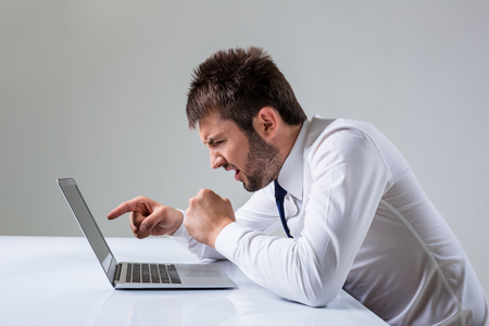 the young man is nervous and poke a finger. It uses a computer while sitting at a table. Office clothingの写真素材