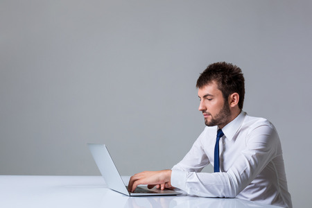 young man smiling at the camera uses a laptop computer while sitting at a table. Office clothing. copyspaceの写真素材