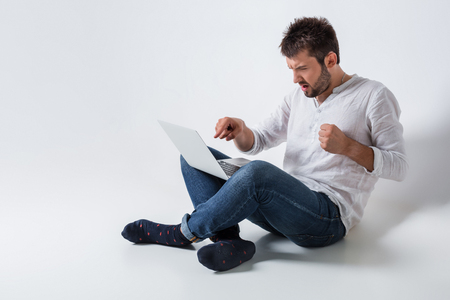 a young man in casual clothes working on a laptop. angry, a slap in the screenの写真素材