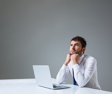 young man thinking uses a laptop computer while sitting at a table. Office clothing. copyspaceの写真素材