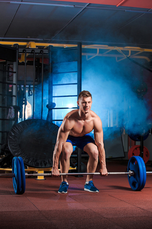 young man doing exercises with barbell in gymの写真素材