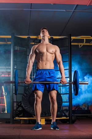 young man doing exercises with barbell in gymの写真素材