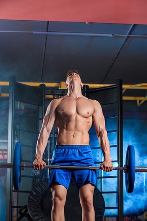 young man doing exercises with barbell in gymの写真素材