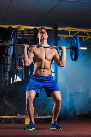 young man doing exercises with barbell in gymの写真素材