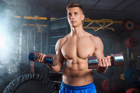 Muscular man doing heavy weight exercise for biceps with dumbbells in modern gymの写真素材