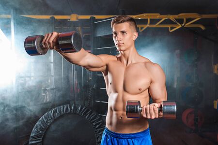 Muscular man doing heavy weight exercise for biceps with dumbbells in modern gymの写真素材