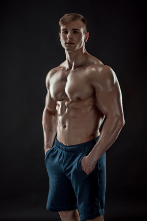 Muscular bodybuilder guy doing posing over black background. Naked torso in jeans. He looks into the cameraの写真素材
