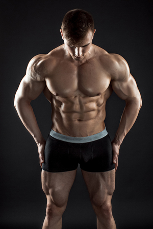 Muscular bodybuilder guy doing posing over black background. Naked torso in shorts.の写真素材