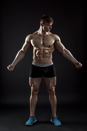 Muscular bodybuilder guy doing posing over black background. Naked torso in shorts. full heightの写真素材