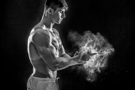 young muscular man preparing to hand lifting heavy weight. White talcum dynamically scatters in different directions. Black and white. stands sidewaysの写真素材