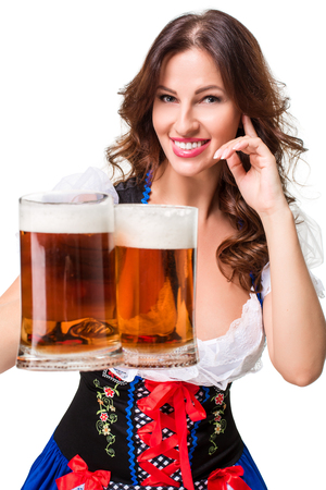 Beautiful young brunette girl in dirndl drinks out of oktoberfest beer stein. Isolated on white background.の写真素材