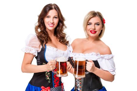 Two beautiful young blond and brunette girls in dirndl drinks out of oktoberfest beer stein. Isolated on white background.の写真素材