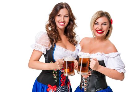 Two beautiful young blond and brunette girls in dirndl drinks out of oktoberfest beer stein. Isolated on white background.の写真素材