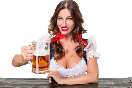 Beautiful young brunette girl in dirndl drinks out of oktoberfest beer stein. Isolated on white background. sits by the tableの写真素材
