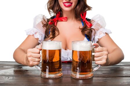 Beautiful young brunette girl in dirndl drinks out of oktoberfest beer stein. Isolated on white background. sits by the table. close up a mugsの写真素材