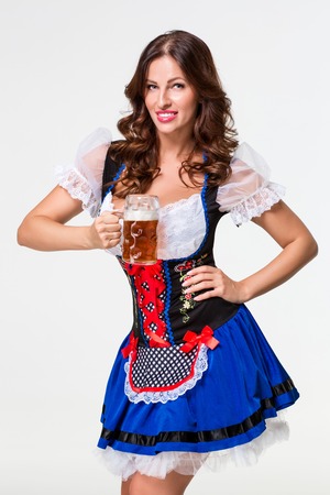 Beautiful young brunette girl in dirndl drinks out of oktoberfest beer stein. on white background.の写真素材