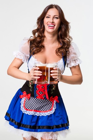 Beautiful young brunette girl in dirndl drinks out of oktoberfest beer stein. on white background.の写真素材