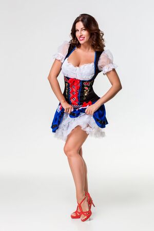 Beautiful young brunette girl in dirndl drinks out of oktoberfest beer stein. on white background. full-lengthの写真素材