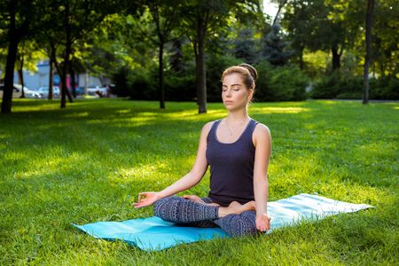 Meditating woman in meditation in city park in yoga pose. Girl relaxing with serene relaxed expression outside in summer. Beautiful young Caucasian female model.の写真素材