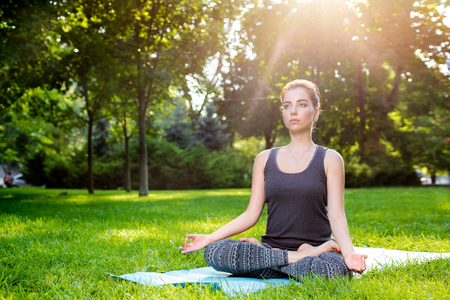 Meditating woman in meditation in city park in yoga pose. Girl relaxing with serene relaxed expression outside in summer. Beautiful young Caucasian female model. sun flareの写真素材