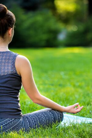 Meditating woman in meditation in city park in yoga pose. Girl relaxing with serene relaxed expression outside in summer. Beautiful young Caucasian female model. Close upの写真素材