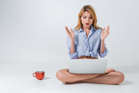 young woman sitting on the floor with crossed legs and using laptop on white background. Surprised, emotionalの写真素材