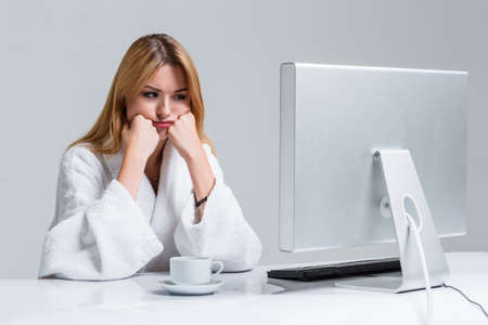 young woman sitting in the table and using computer on gray background. sleepy in the morning looking at the monitorの写真素材
