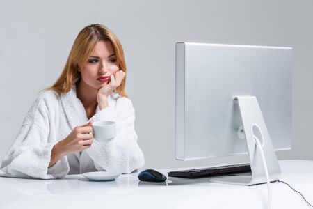 young woman sitting in the table and using computer on gray background. sleepy in the morning looking at the monitorの写真素材