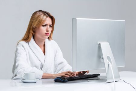 young woman sitting in the table and using computer on gray background. sleepy in the morning looking at the monitorの写真素材