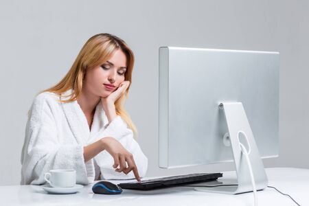 young woman sitting in the table and using computer on gray background. sleepy in the morning looking at the monitorの写真素材