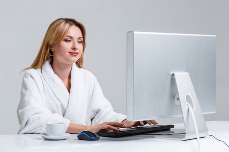 young woman sitting in the table and using computer on gray background. girl smiling and looking at monitorの写真素材