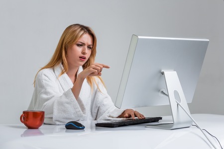 young woman sitting in the table and using computer on gray background. indignation is pointing at the monitorの写真素材