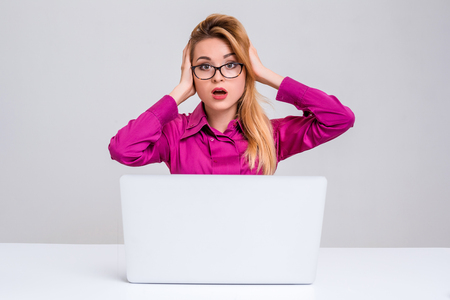 Young businesswoman working at laptop computer. she is going through and looking at the camera. her head in her handsの写真素材