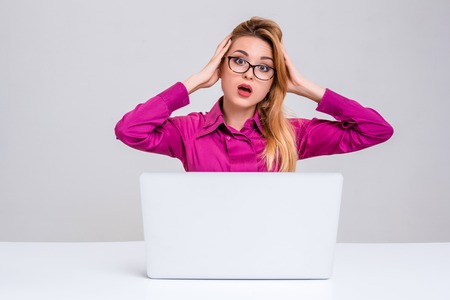 Young businesswoman working at laptop computer. she is going through and looking at the camera. her head in her handsの写真素材